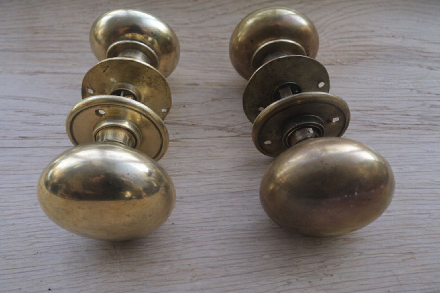 Twee paar klassieke messing deurknoppen op een houten ondergrond.