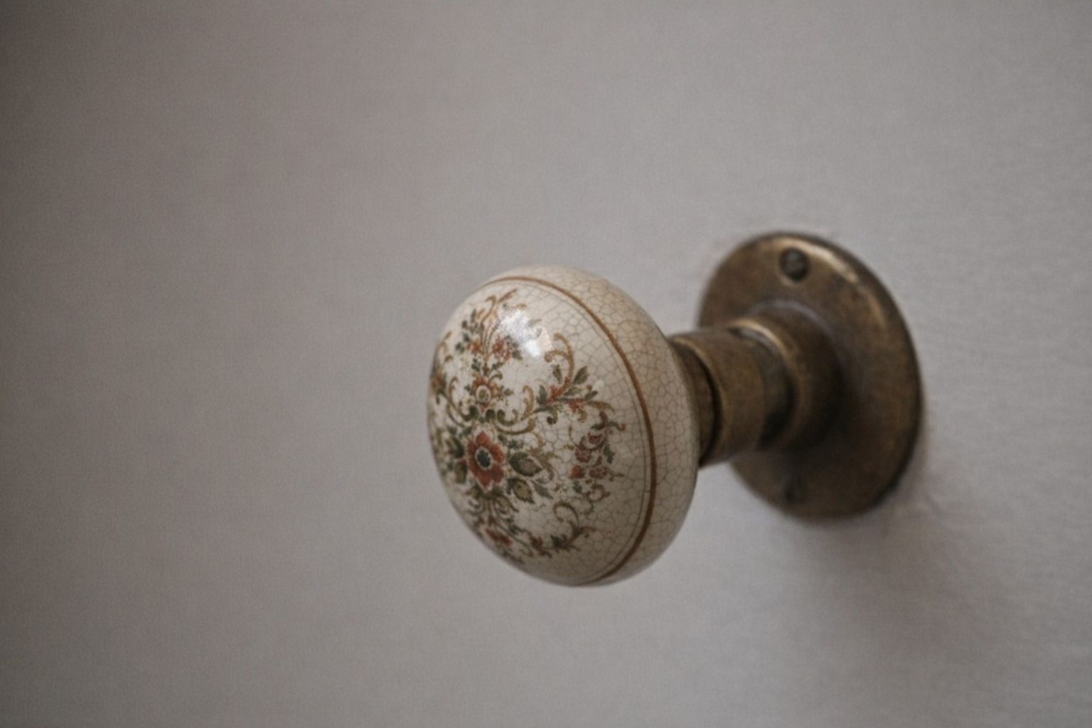 Antieke porseleinen binnendeurknop met bloemmotief en koperen beslag.