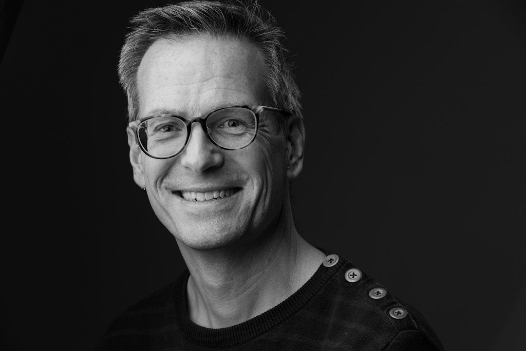 Zwart-witportret van een glimlachende man met bril en donkere trui
